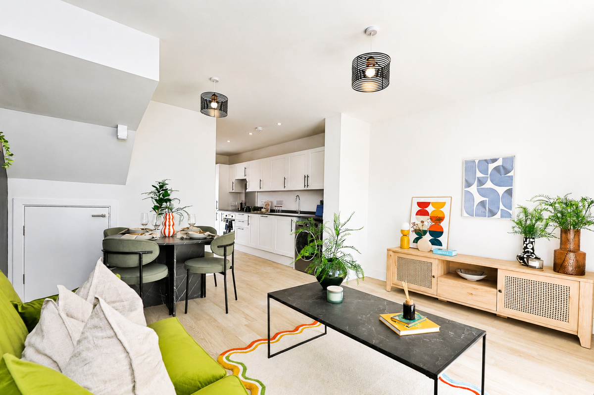Bright modern open plan living room with lime green sofa cushions black coffee table dining area white kitchen wooden sideboard plants and abstract wall art